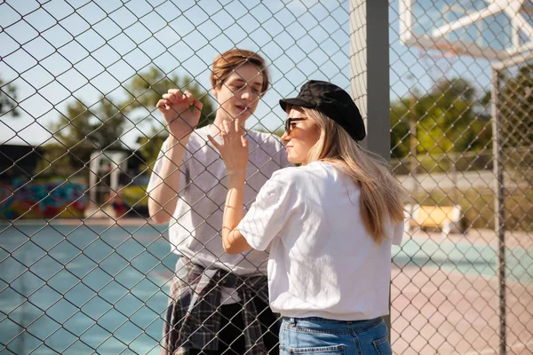 Porträt eines jungen schönen Paares, das sich durch einen Maschendrahtzaun betrachtet. nachdenklicher Junge steht auf Basketballplatz und schaut hübsches Mädchen an, während sie verträumt zur Seite schaut — Stockfoto