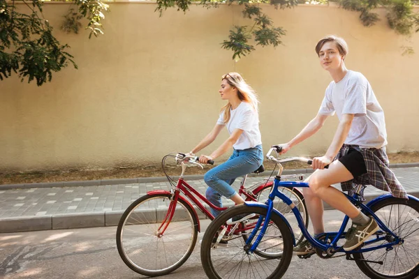 멋진 소년 예쁜 여자와 함께 자전거를 타고 하는 동안 카메라를 찾고 행복 하 게. 도시의 거리에 따라 빨간색과 파란색 자전거를 타고 하는 동안 함께 시간을 보내는 젊은 커플의 사진 — 스톡 사진