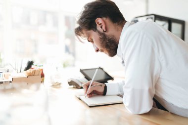 Genç adam beyaz gömlekli defter Restoran sayacında işyerinde üzerinde yazılı. Barista düşünceli kafede işyerinde notlar yapma. İşyeri kafede üzerinde genç barista portresi