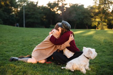 Çimenlerin üzerinde oturan ve onların küçük sevimli köpek park ile vakit iki genç güzel Bayan portresi