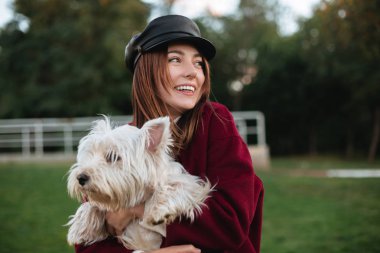Siyah kap ve parkta duran ve sonsuza dek mutlu bir kenara onun küçük sevimli köpek elinde tutarken seyir ceket gülümseyen güzel Bayan portresi