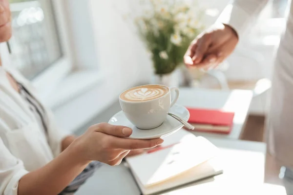 Närbild av kvinna hand tar kaffekopp från mannen hand i kafé. Porträtt av handen håller vit kopp cappuccino i restaurang — Stockfoto