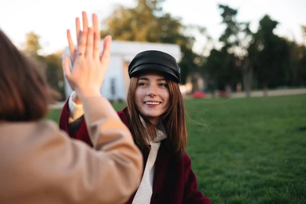 Feche a foto da linda senhora sentada na grama e dando cinco para sua amiga enquanto feliz passar o tempo no parque — Fotografia de Stock