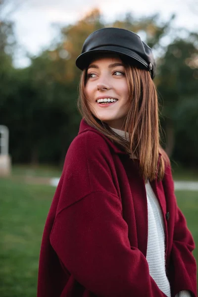 Ritratto di bella ragazza in berretto nero e cappotto in piedi nel parco e gioiosamente guardando da parte isolato — Foto Stock