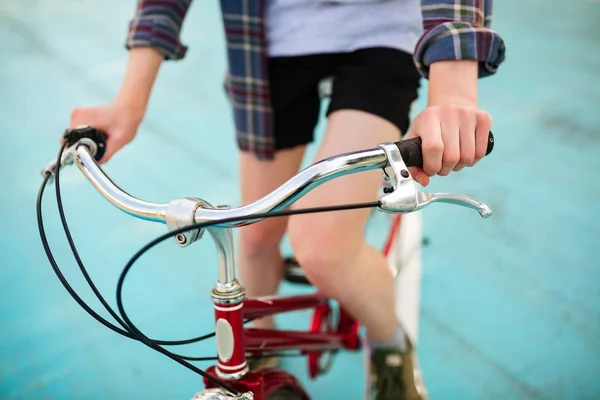 Foto de cerca del cuerpo del joven montando bicicleta roja en el parque. Foto de bicicleta roja clásica en cancha de baloncesto — Foto de Stock