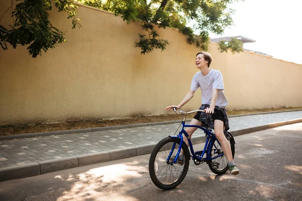 Portrét se chlapcem radostně jízda kole. Veselý mladík s plavými vlasy, baví se při jízdě na modrém kole podél ulice — Stock fotografie