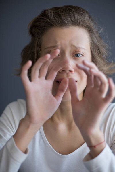 Portrait of young frightened lady sadly looking in camera while holding hands in front of her face isolated