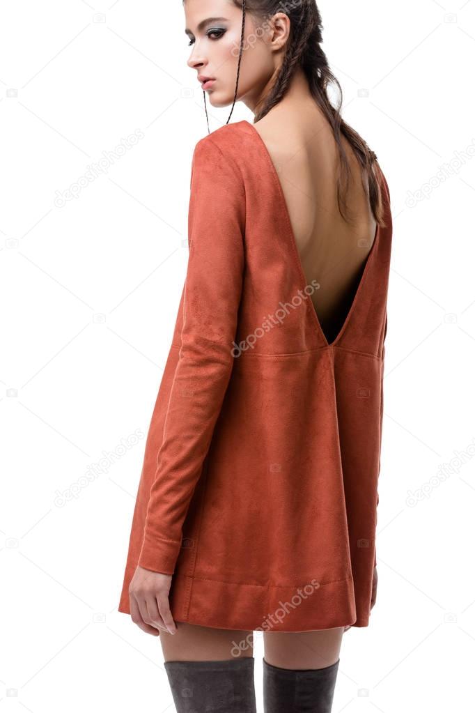 Pretty young lady standing from back in ginger suede dress with cut on back and knee high boots on white background