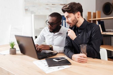 Masada oturan ve düşünceli laptop ile birlikte izole ofisinde çalışan iki genç çokuluslu işadamları portresi