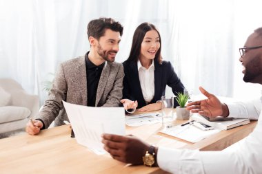 Genç gülümseyen çok uluslu iş adamları ve masada oturan ve Office birlikte çalışma sırasında yeni proje tartışıyor işkadını portre