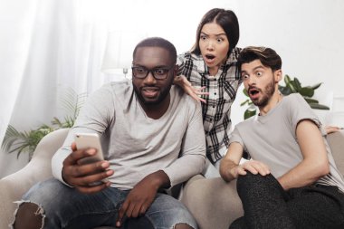Evde ve amazedly hareket eden telefon içinde birlikte izole vakit süre seyir sandalyelere oturan üç şok arkadaş portresi