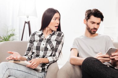 İzole yakınındaki cellphone ile evde oturan genç adam elinde ve indignantly seyir defteri ile sandalyede oturan genç bayan portresi