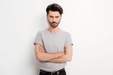 Kahverengi saç ve sakal ayakta ve öfkeyle kamera Studio beyaz arka plan üzerinde seyir ile genç adam portresi
