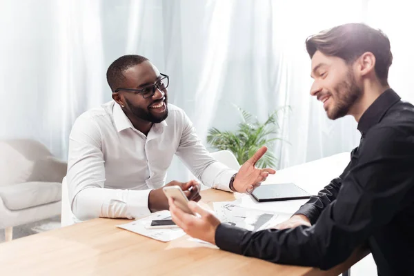 Portrait Two Young Smiling Multinational Businessmen Sitting Table Talking While — Stock Photo, Image