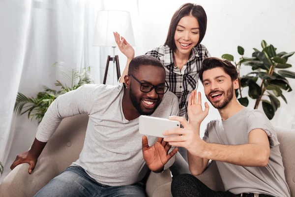 Retrato Tres Amigos Sonrientes Sentados Sillas Casa Saludando Alegremente Gesto —  Fotos de Stock