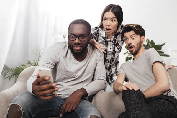 Portrait Three Shocked Friends Sitting Chairs Home Amazedly Looking Mobile — Stock Photo, Image