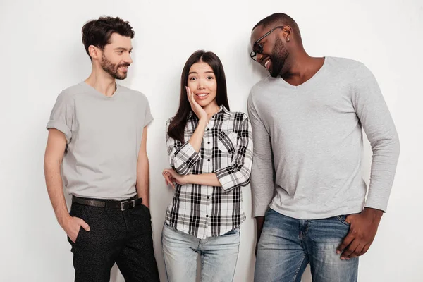 Portrait of two friends standing together and dreamily looking at beautiful girl between them on white background in studio