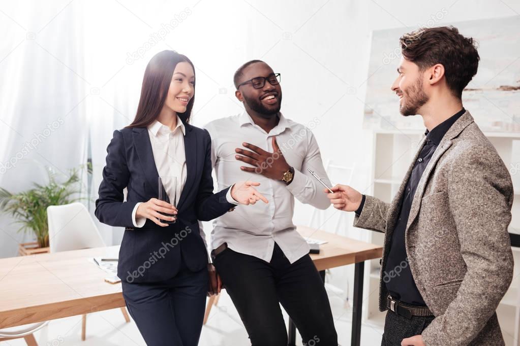 Portrait of happy multinational businessmen and businesswoman standing near table and talking while working together in office isolated