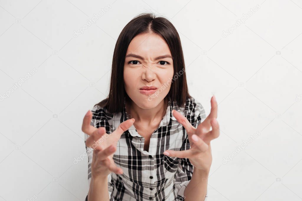 Portrait of grumpy lady with dark hair standing and angrily looking in camera on white background in studio