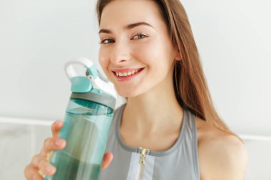 Genç Bayan mutlu kamera seyir kulaklık ve şişe suyu üzerinde izole mutfak elinde ile sportif üst fotoğrafı kapatın