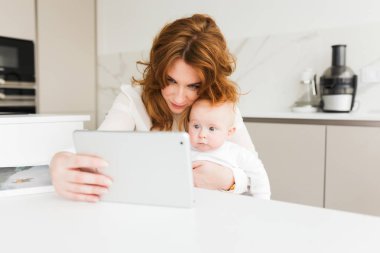 Oturma ve sevimli küçük bebeği elinde sersem arıyor tablet izole tutarken güzel kadın portresi