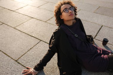 Afrikalı kıvırcık kız siiting açık havada günbatımı arka ışık ve içme ile çatıda portresi kahve götürün