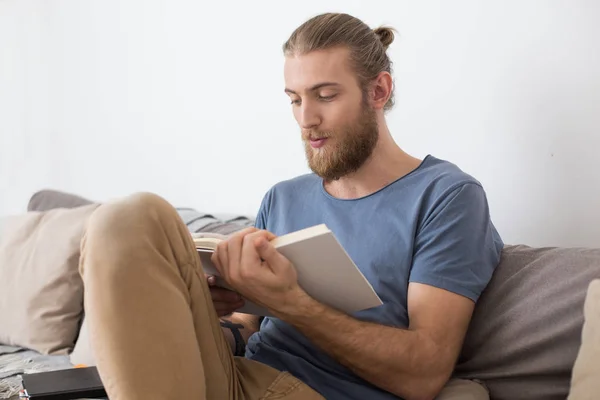 Retrato Joven Sentado Gran Sofá Gris Libro Lectura Casa Aislado — Foto de Stock