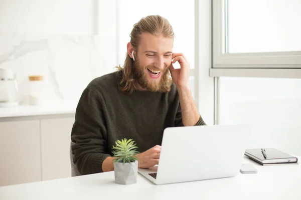 Retrato Joven Hombre Alegre Auriculares Sentados Mesa Riendo Mientras Mira — Foto de Stock