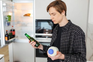 Bira ve süt elinde evde buzdolabı yakınındaki ayakta düşünceli adam portresi izole