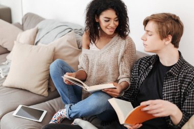 Genç adamla büyük kanepede oturan ve evde birlikte kitap okuma gülümseyen kadın portresi izole