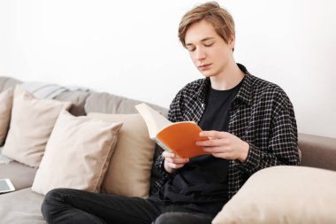 Büyük kanepede oturan ve evde kitap okuma düşünceli adam izole genç portresi