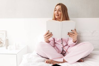 Yatakta kitap el ile oturma ve sersem bir kenara eve izole bakarak güzel Bayan