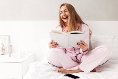 Yatakta kitap el ile oturan ve evde gülerek mutlu kadın portresi izole