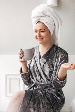 İzole kadife bornoz havlu kafa ve evde yardım kadehte ile oturan güzel Bayan portresi