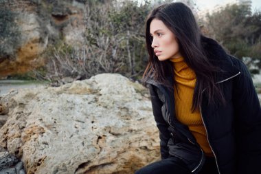 Ceketli güzel Asyalı esmer kızın yan görünüşü. Dışarıdaki taşlara güvenle bakıyor.