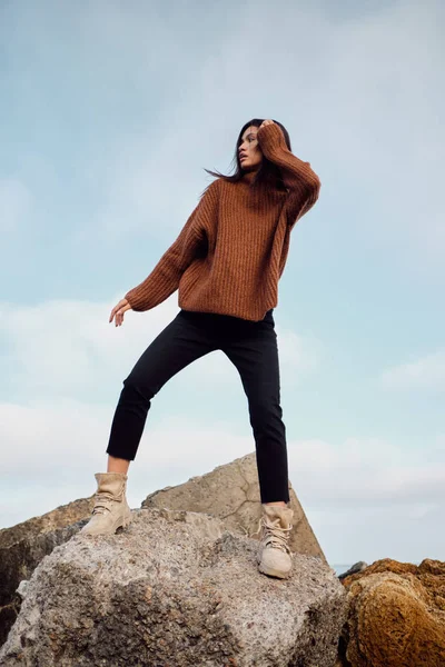 Красивая случайная азиатка в уютном трикотажном свитере позирует на больших камнях на берегу моря — стоковое фото