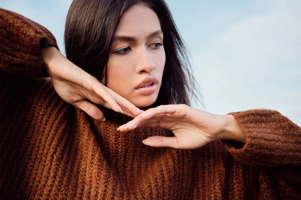 Close up attractive Asian brunette girl in knitted sweater thoughtfully posing outdoor — Stock Photo, Image