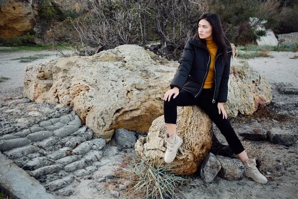 Belle fille brune asiatique décontractée en duvet regardant attentivement loin sur les pierres en plein air — Photo