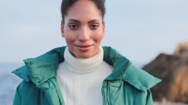 Çekici Afro-Amerikan kızı deniz kenarındaki kameraya bakarken mutlu oluyor.