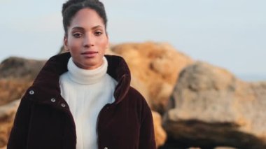 Oldukça sıradan bir Afrikalı Amerikalı kız. Ceketli, kendinden emin bir şekilde kameraya bakıyor ve kumsalda gülümsüyor.