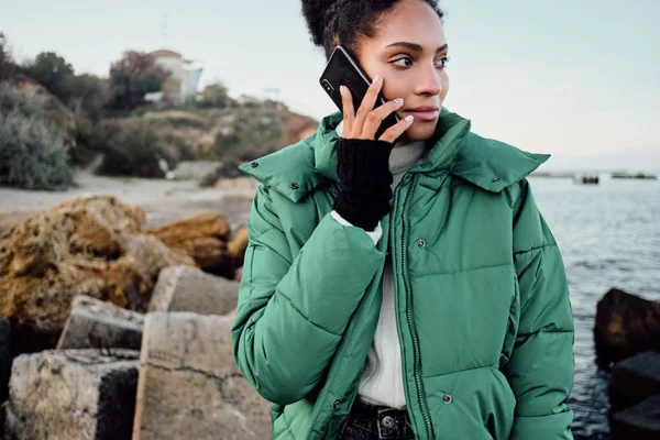 美しいですカジュアルアフリカ系アメリカ人の女の子でダウンジャケット上の携帯電話で話す海 — ストック写真