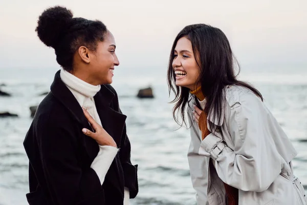 Zwei fröhliche, lässige Mädchen, die fröhlich miteinander reden, wenn sie am Meer spazieren gehen — Stockfoto