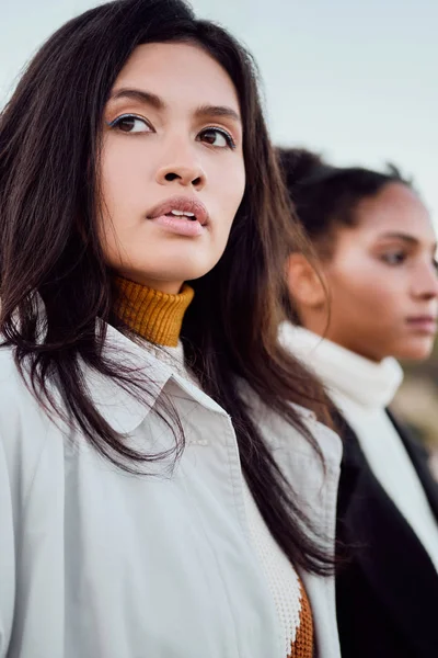 Beautiful Asian girl thoughtfully looking away standing with African American friend by the sea — Stock Photo, Image