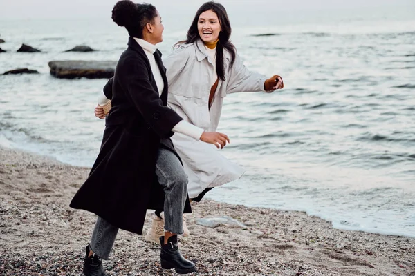 Zwei schöne stilvolle Mädchen in Trenchcoats glücklich am Meer entlang laufen — Stockfoto