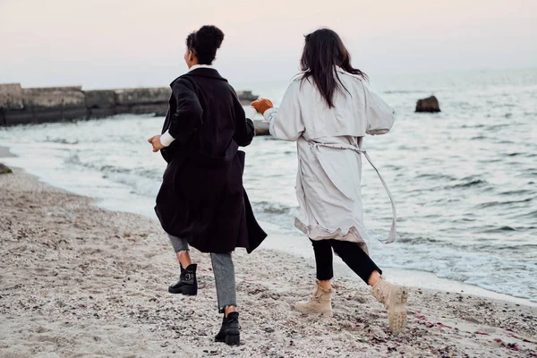 Widok z tyłu dwóch atrakcyjnych stylowych dziewcząt w płaszczach kąpielowych szczęśliwie biegających nad morzem — Zdjęcie stockowe