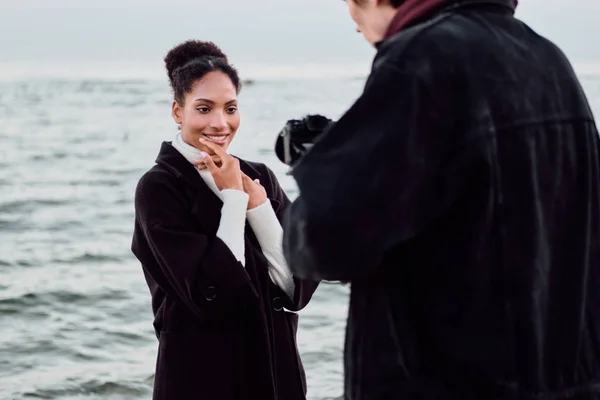 Красивая улыбающаяся афроамериканка счастливо позирует перед камерой во время фотосессии у моря — стоковое фото