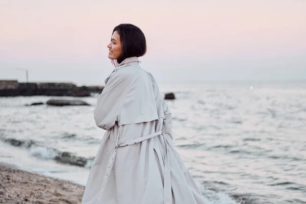 Takaisin näkymä melko tyylikäs aasialainen tyttö trench takki onnellisesti kävely meren rannalla — kuvapankkivalokuva