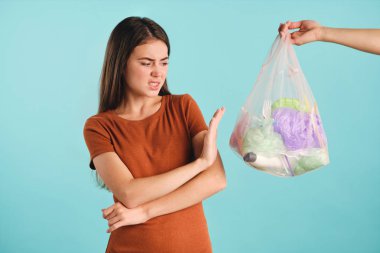 Üzgün kız titizlikle hiç hareket göstermeden renkli arkaplanda plastik atık dolu bir çantaya bakıyor.