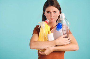Elinde boş plastik deterjanlar tutan sinirli kız renkli arka planda kameraya bakıyor.