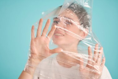 Plastik torba içinde boğulan üzgün bir kız. Üzücü bir şekilde renkli arka plan üzerinden kameraya bakıyor. 
